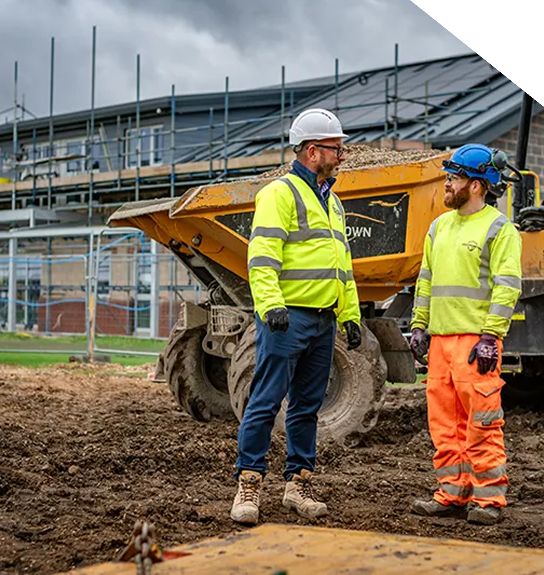 Two grounds-workers mid-conversation, standing in front of a forward tipping dumper.