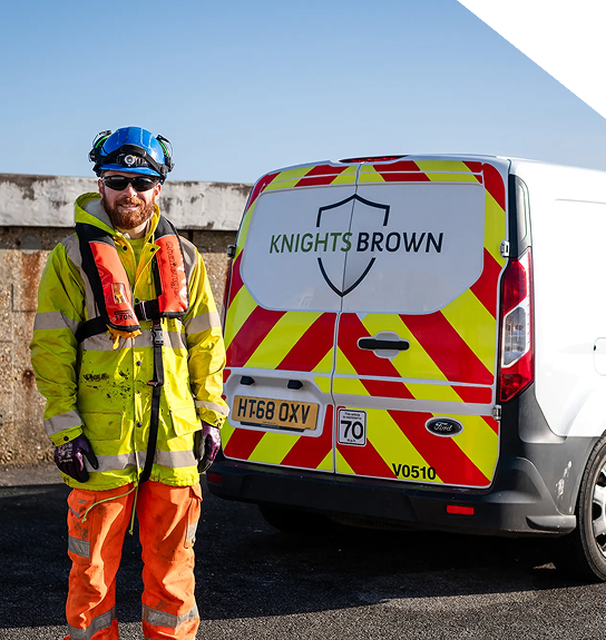 A highways technician standing infront of the back of his parked van, wearing a high vis jacket.